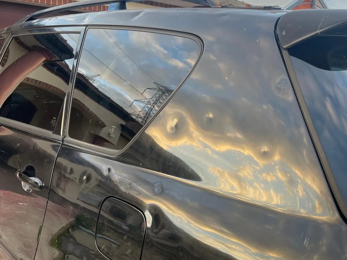 Deep hail dents across the rear quarter panel and roof rail of a black Toyota removed in Perth